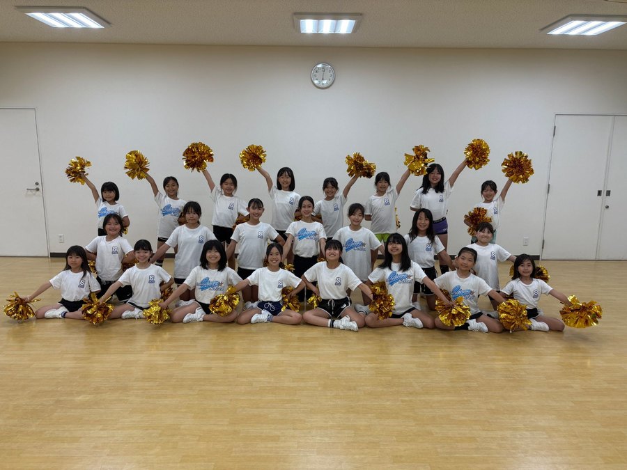 金色のポンポンを持って笑顔でポーズをとるレイクスチアスクールの子どもたちの集合写真